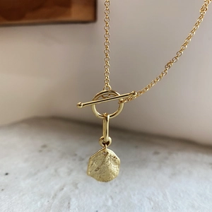 Detail of golden OT clasp necklace with irregular textured pendant on a sand surface