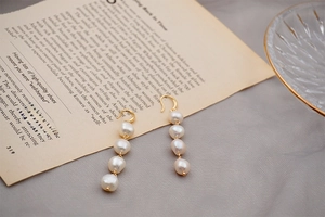 Macro detail of long freshwater baroque pearl earrings on vintage book page background