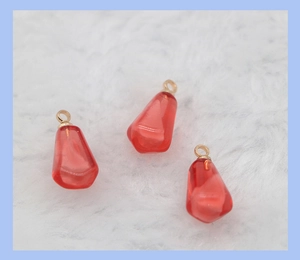 Detail view of red resin pomegranate seeds with gold loops on white plush background