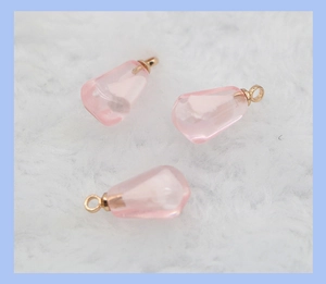 Macro detail of three pink teardrop resin charms with gold metal loops on soft fur