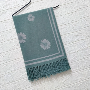 Detail of dark green knit scarf with grey floral jacquard pattern and fringe trim