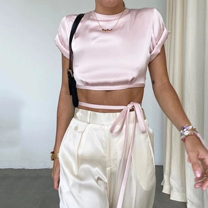 Detail of pink satin crop top featuring a criss-cross waist tie and rolled short sleeves