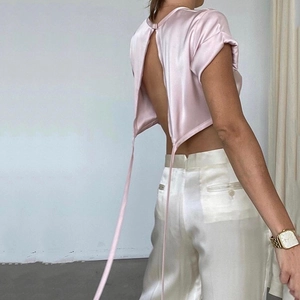 Pink satin backless crop top with long wrap ties and matching white silk trousers