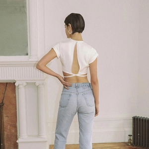 Detail view of white backless crop top featuring criss-cross lace-up design and blue jeans