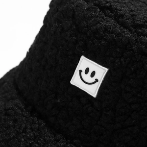 Thick black teddy fleece bucket hat with a white smiley face patch and cozy texture