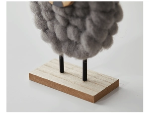 Close-up of wool felt sheep ornament with thin black metal legs on a wooden base