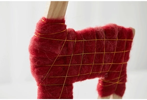 Macro view of handmade red wool reindeer ornament with gold thread on wooden frame