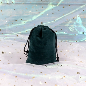 Detailed view of a dark green velvet drawstring pouch on a decorative background