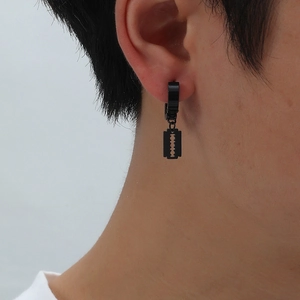 Close-up of a black stainless steel razor blade pendant earring worn on a male ear