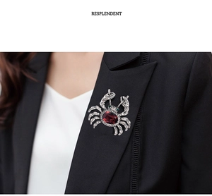 Detailed view of a silver crab brooch with a red gemstone on a black suit lapel