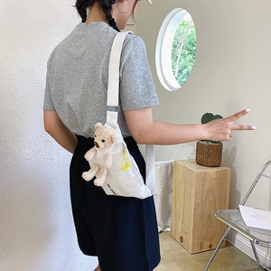 Detail of white canvas chest bag featuring a brown teddy bear charm and yellow zipper puller