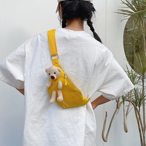 Detail of yellow canvas crossbody bag with cute plush bear charm and printed logo