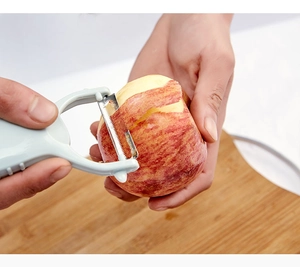 Close-up of a blue dual-head peeler with serrated blade peeling a red apple on a board