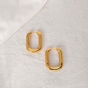 Close-up of golden U-shaped oval hoop earrings on white textured fabric background