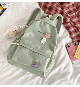 Detailed view of green canvas backpack with cute bear pendant and cartoon badges on bedding