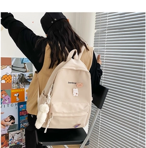 Detail of a minimalist off-white backpack featuring cute plush animal charms and pins
