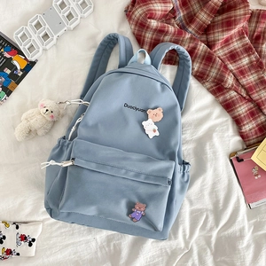 Detail view of blue canvas school backpack with cute bear pendant and pins on bedsheets