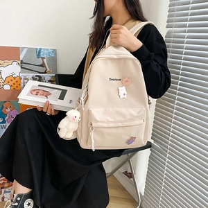 Detail of beige backpack with cute bear patches and plush keychain shown on a model