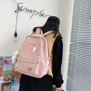Detailed view of pink nylon backpack with cute bear badges and a plush bear keychain charm