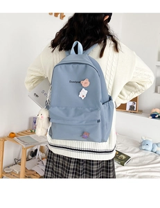 Blue canvas backpack featuring cute bear badges and a white plush charm on a female model