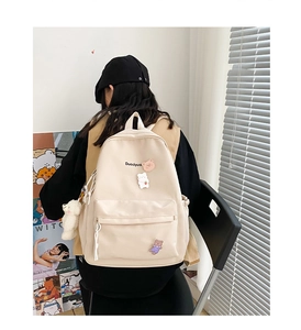 Detail of off-white canvas backpack featuring cute bear charms and letter embroidery