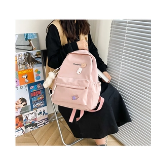 Pink nylon backpack with cute bear badges and white plush charm in close-up detail