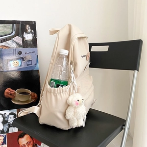 Detail view of beige canvas backpack with water bottle pocket and cute plush teddy bear