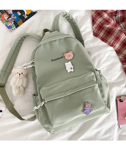 Flat lay of light green nylon school bag with cute bear pendant and badges on white sheets