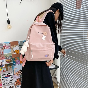 Detail view of pink fabric backpack featuring a cute cartoon bear pin and plush pendant