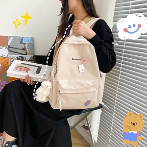 Detail of cute beige canvas backpack with bear charm and Duociyuar logo on model
