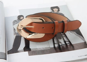Detail of a brown leather belt with a large polished gold metal buckle on a fashion magazine