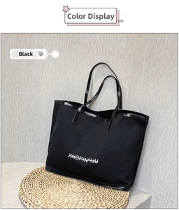 Detail of black canvas tote bag on woven mat featuring faux leather straps and logo