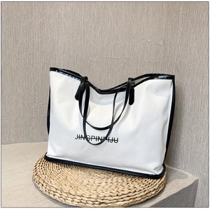 Detailed close-up of white tote bag with black trim and handles on woven mat