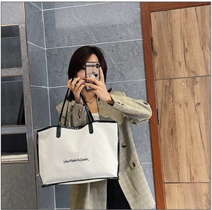 Mirror selfie showing a large white tote bag with black straps and letter print detail
