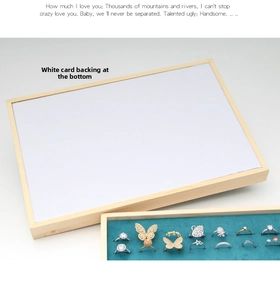 Detail of wooden jewelry tray featuring teal velvet ring slots and white card lining