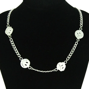 Detail of silver chain necklace featuring round smile and sad face emojis on black bust