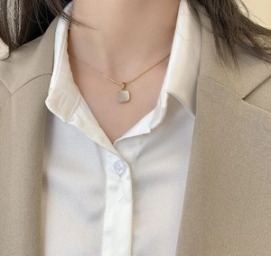 Detail of square white mother-of-pearl pendant necklace on a gold chain worn by a model