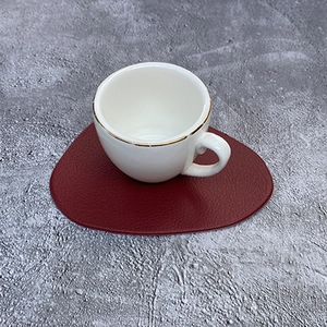 Roter tropfenförmiger Kunstleder-Untersetzer mit weißer Kaffeetasse mit Goldrand