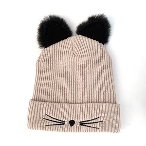 Close-up of beige knit hat featuring plush black cat ears and embroidered whiskers detail