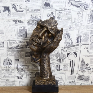 Abstract bronze resin sculpture of thinking face on black base with golden texture
