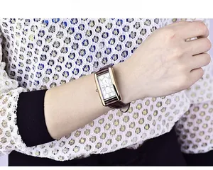 Detail of a vintage square watch with Roman numerals and brown leather strap on a wrist