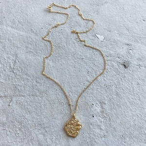 Close-up of golden irregular lion head embossed pendant necklace on textured background