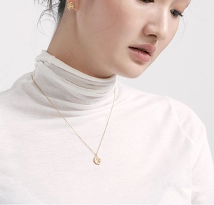 Detail of a minimalist gold irregular pendant necklace and earrings set on a model