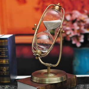 European vintage rotating brass hourglass timer with white sand on a wooden base