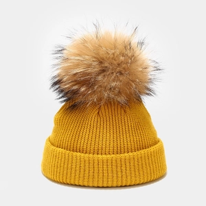 Close-up of yellow knit beanie with fluffy faux fur pom-pom and ribbed texture