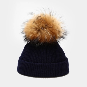 Detail of navy knit baby hat featuring chunky ribbed texture and a fluffy brown fur pompom