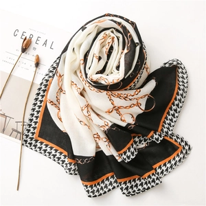 Dettaglio di un'elegante sciarpa con motivo pied de poule e stampe a catena dorata in arancio e nero