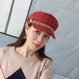 Detail of red tweed newsboy hat with gold chain accent worn by a female model