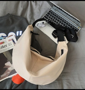 Beige nylon hobo bag shown in a casual lifestyle setting with accessories and laptop