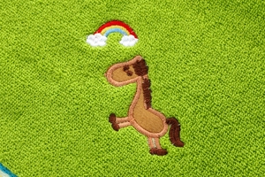 Macro view of bright green cotton towel featuring rainbow and pony embroidery details
